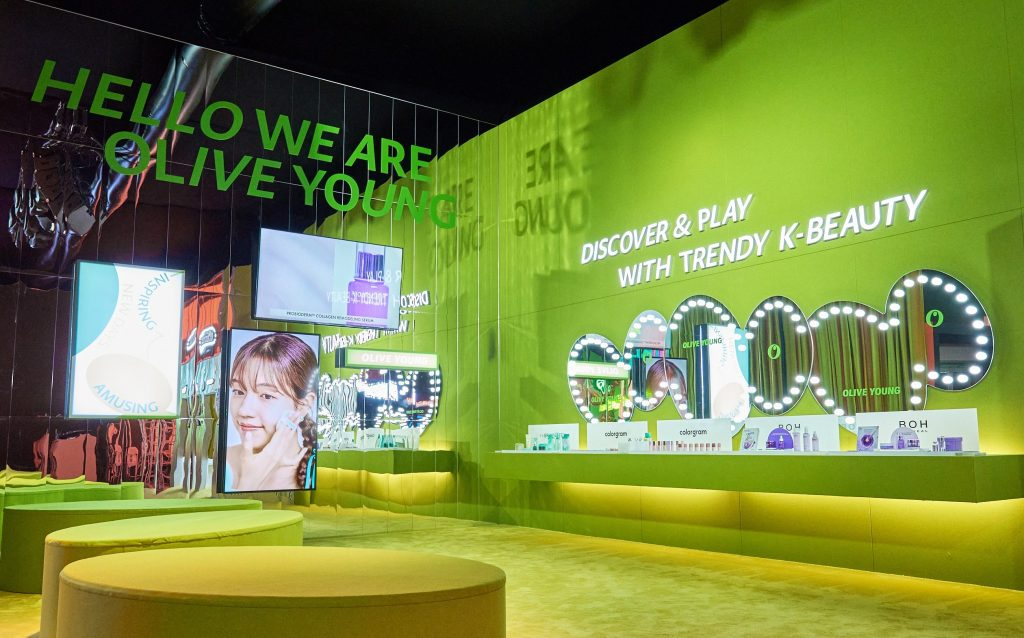 A bright green Olive Young beauty booth features product displays, illuminated signage, and seating.