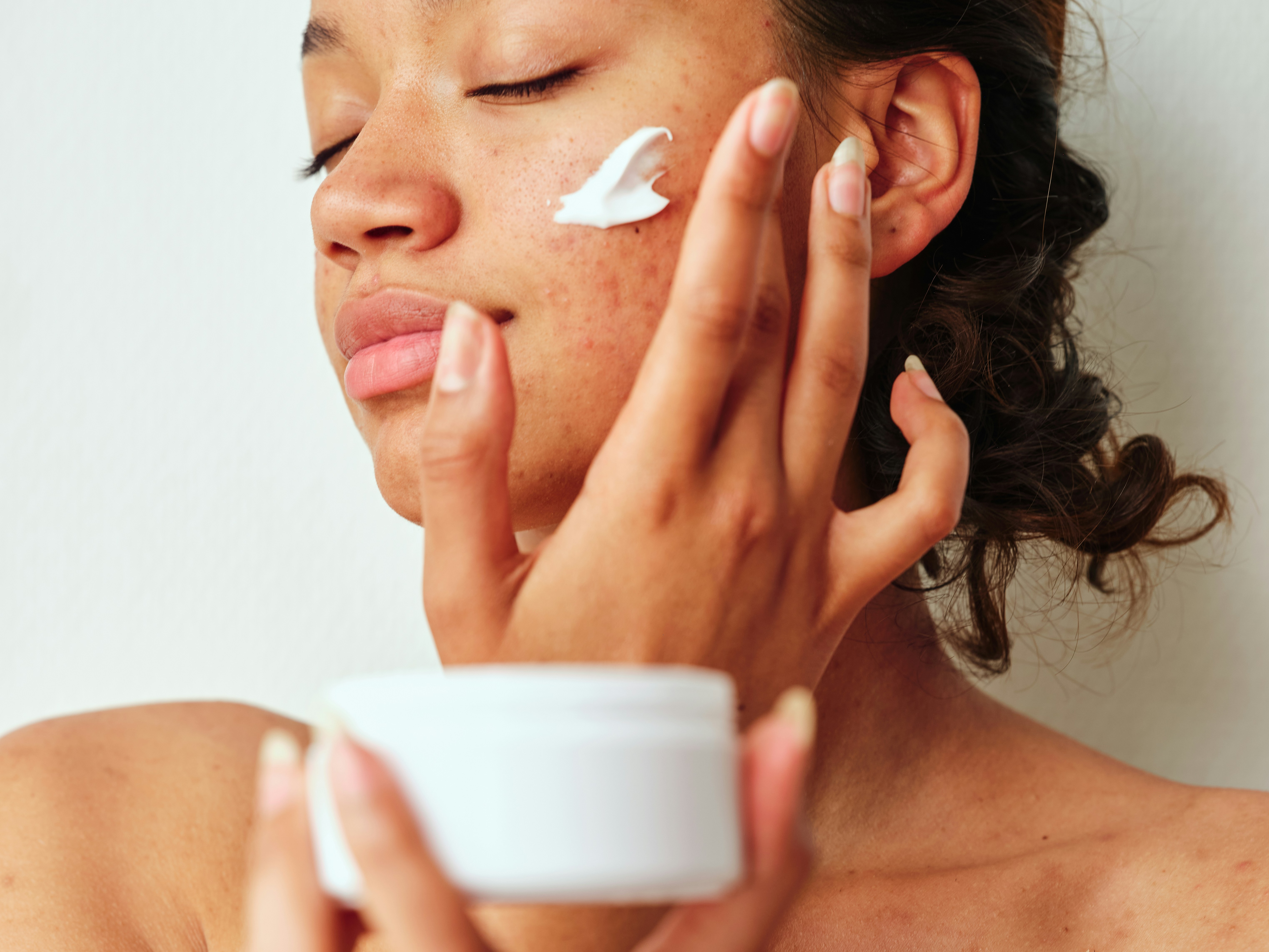 A person applies white cream to their cheek with their fingers.