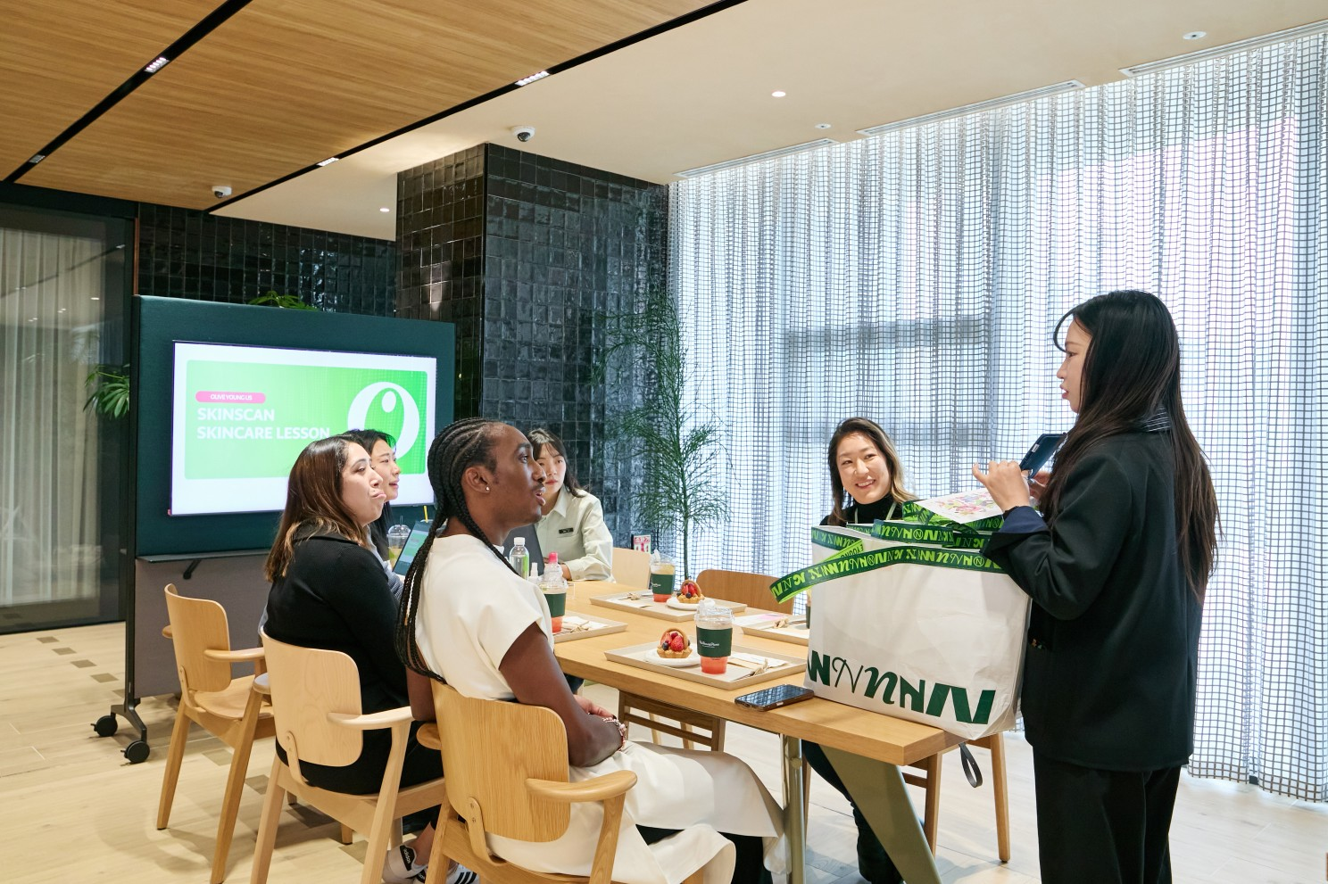 Several people attend a skincare lesson as a presenter holds a large branded bag.