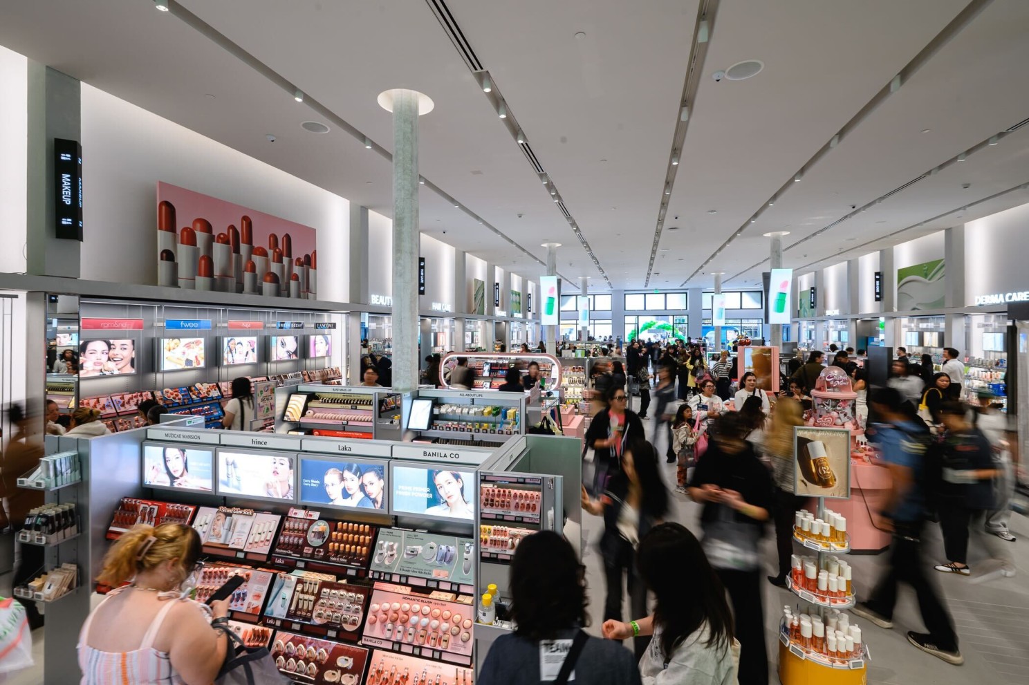A crowded cosmetics store displays makeup and skincare products beneath bright lights.