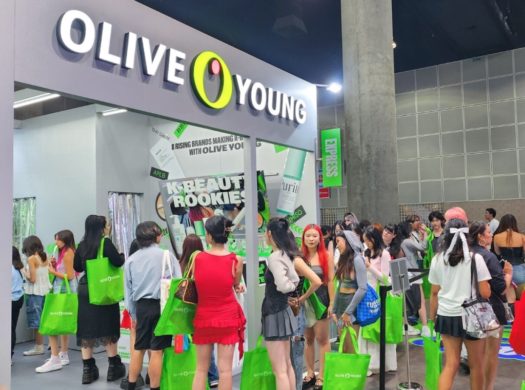 Crowds gather at an Olive Young beauty booth, carrying bright green shopping bags.