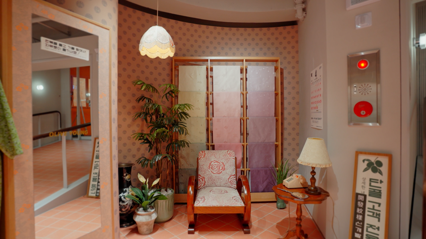 A vintage sitting area has a floral armchair, plants, a lamp, and a telephone.