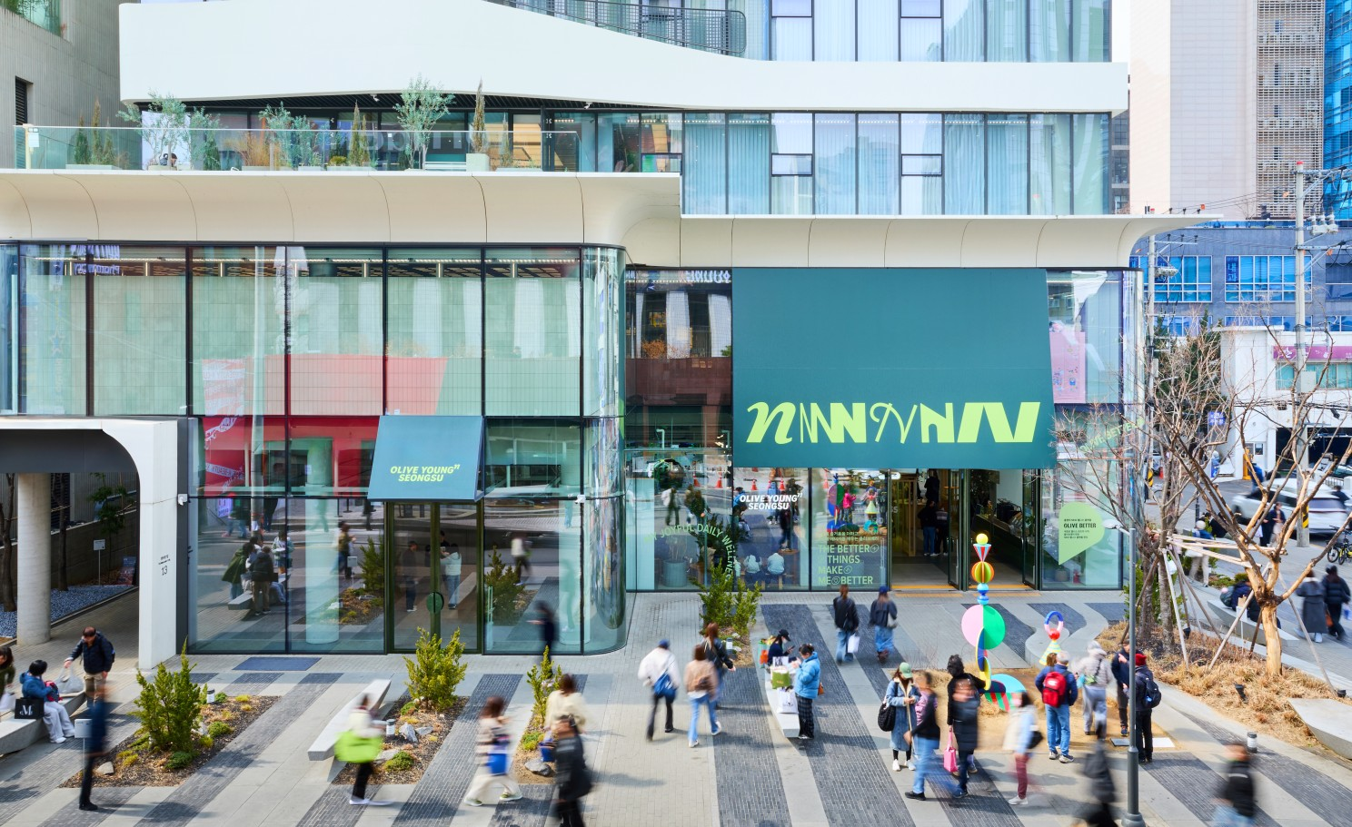 People walk past an Olive Young storefront in a modern shopping district.
