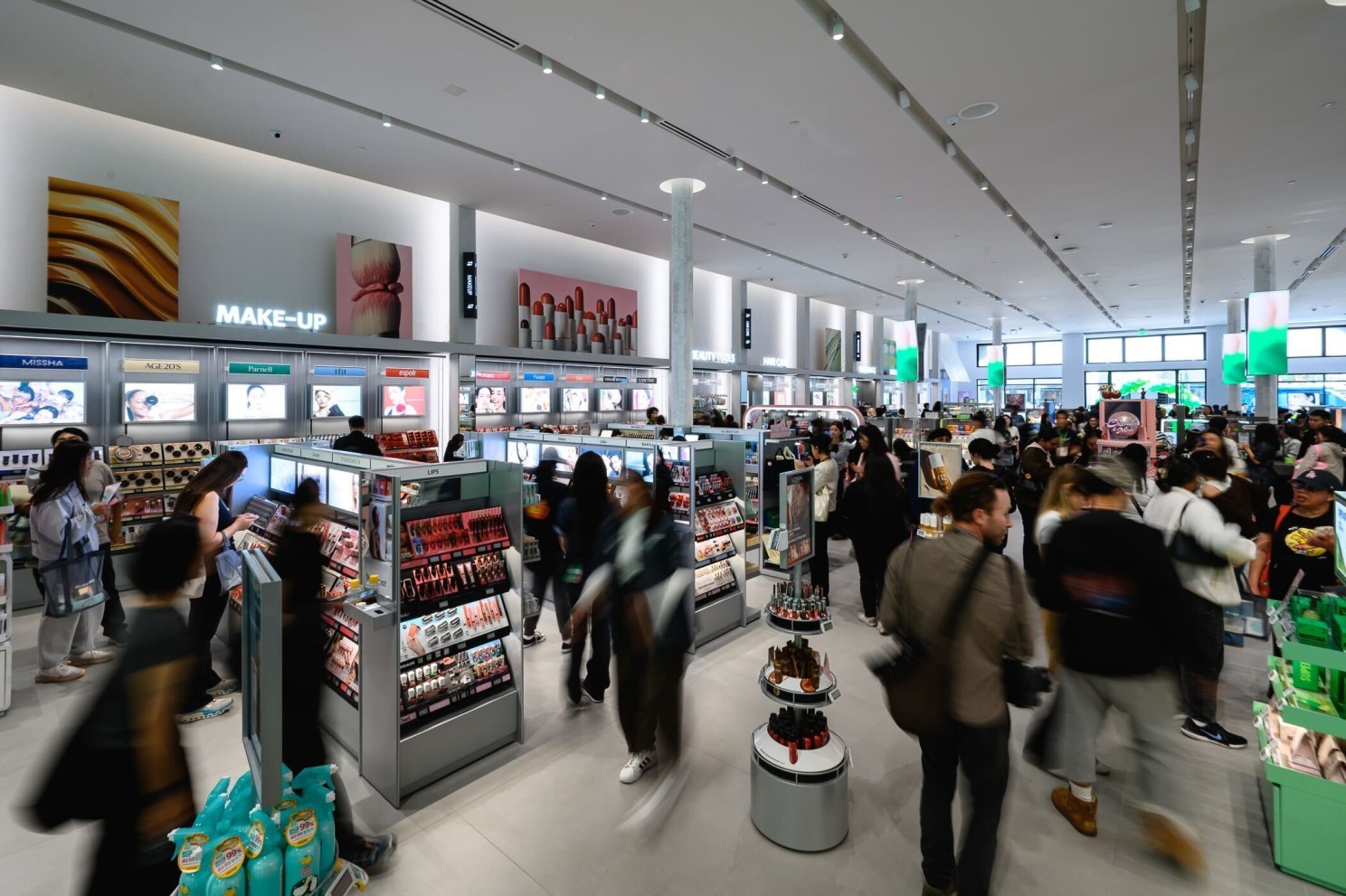 Busy cosmetics store with shoppers browsing makeup displays and shelves.