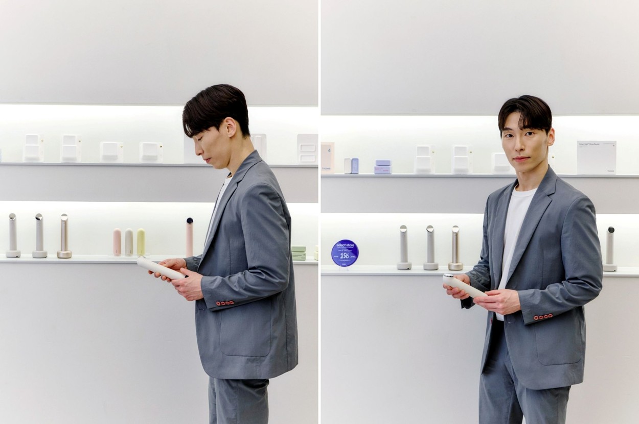 A man in a gray suit holds a white device in a bright showroom, shown from two angles.