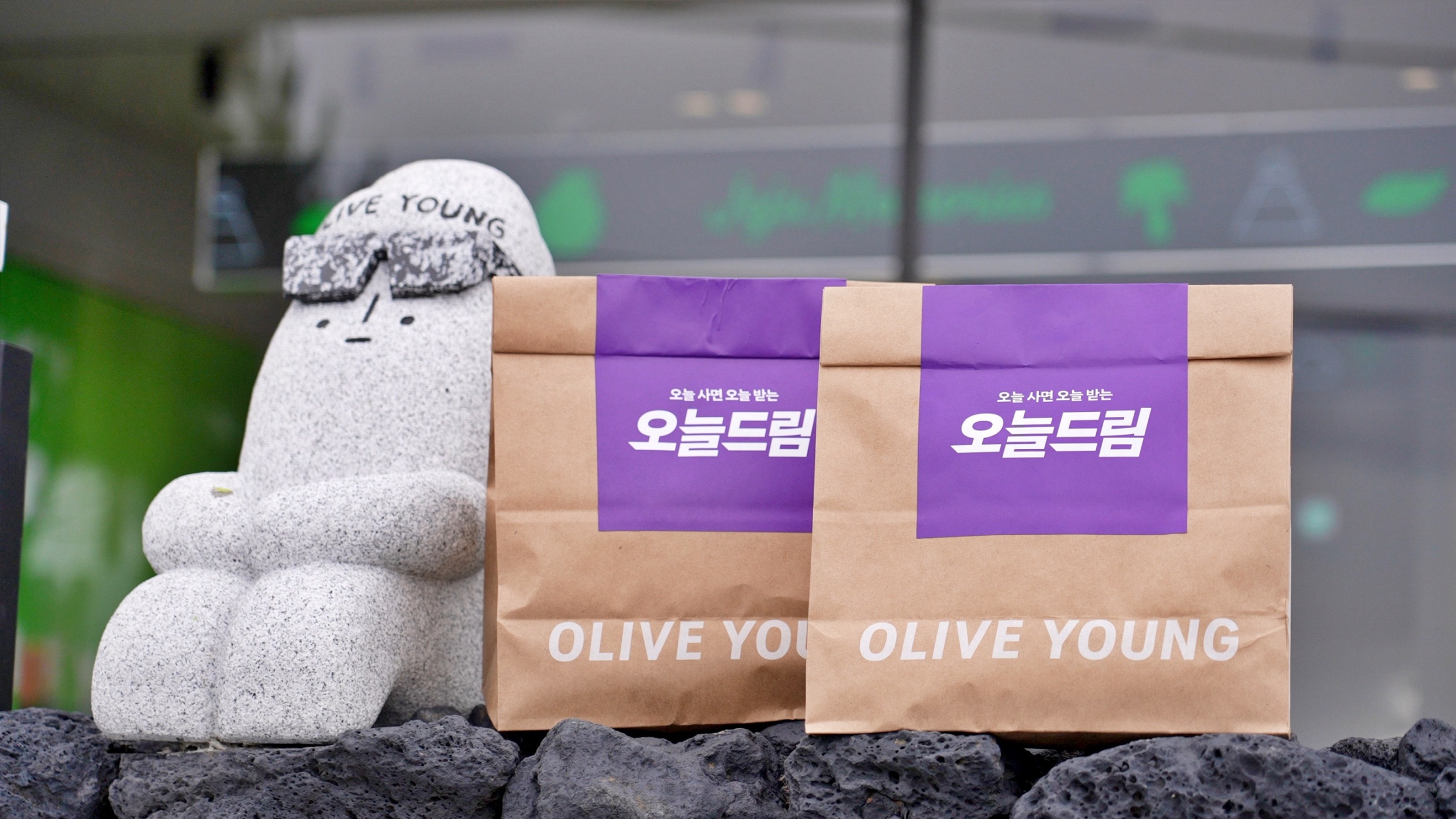 A stone rabbit statue sits beside two paper bags labeled OLIVE YOUNG.