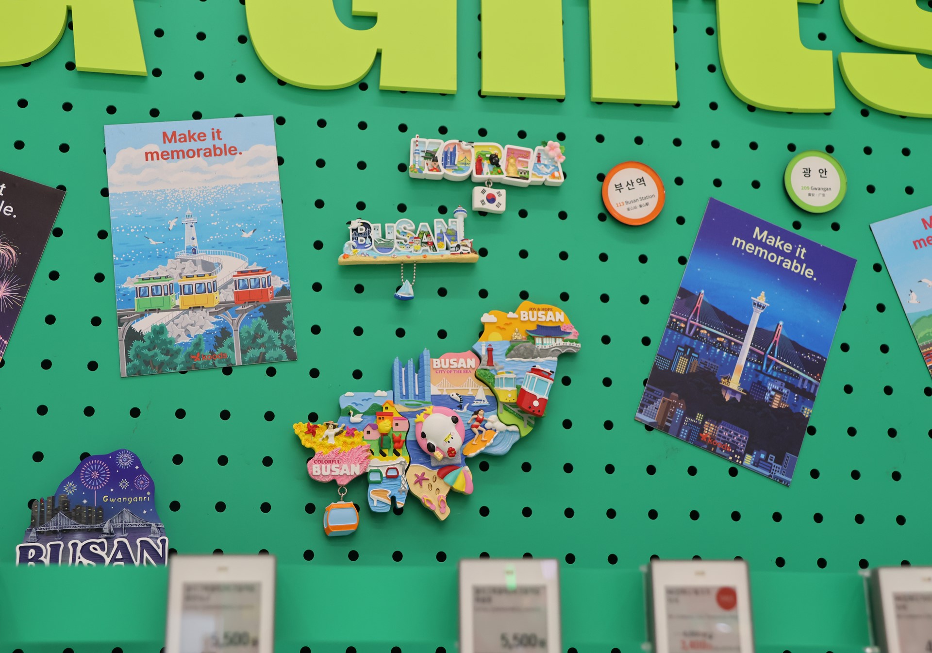 Busan souvenirs, including postcards and colorful magnets, hang on a green pegboard.