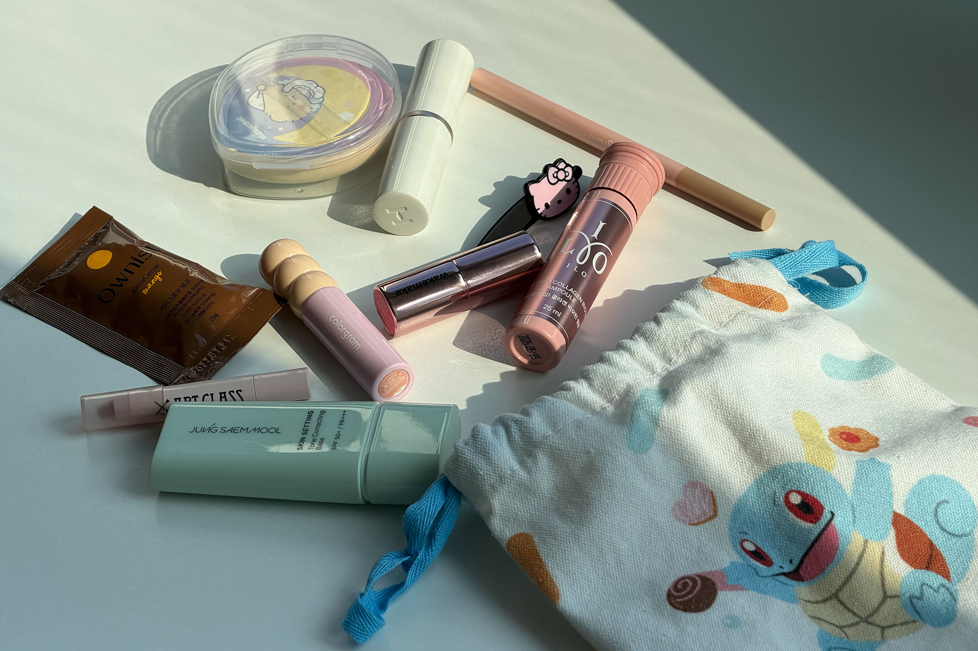 Makeup products and a colorful drawstring pouch sit on a sunlit surface.