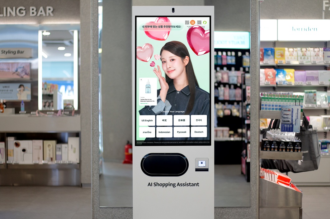 A store kiosk labeled “AI Shopping Assistant” displays a woman and language options at OLIVE YOUNG