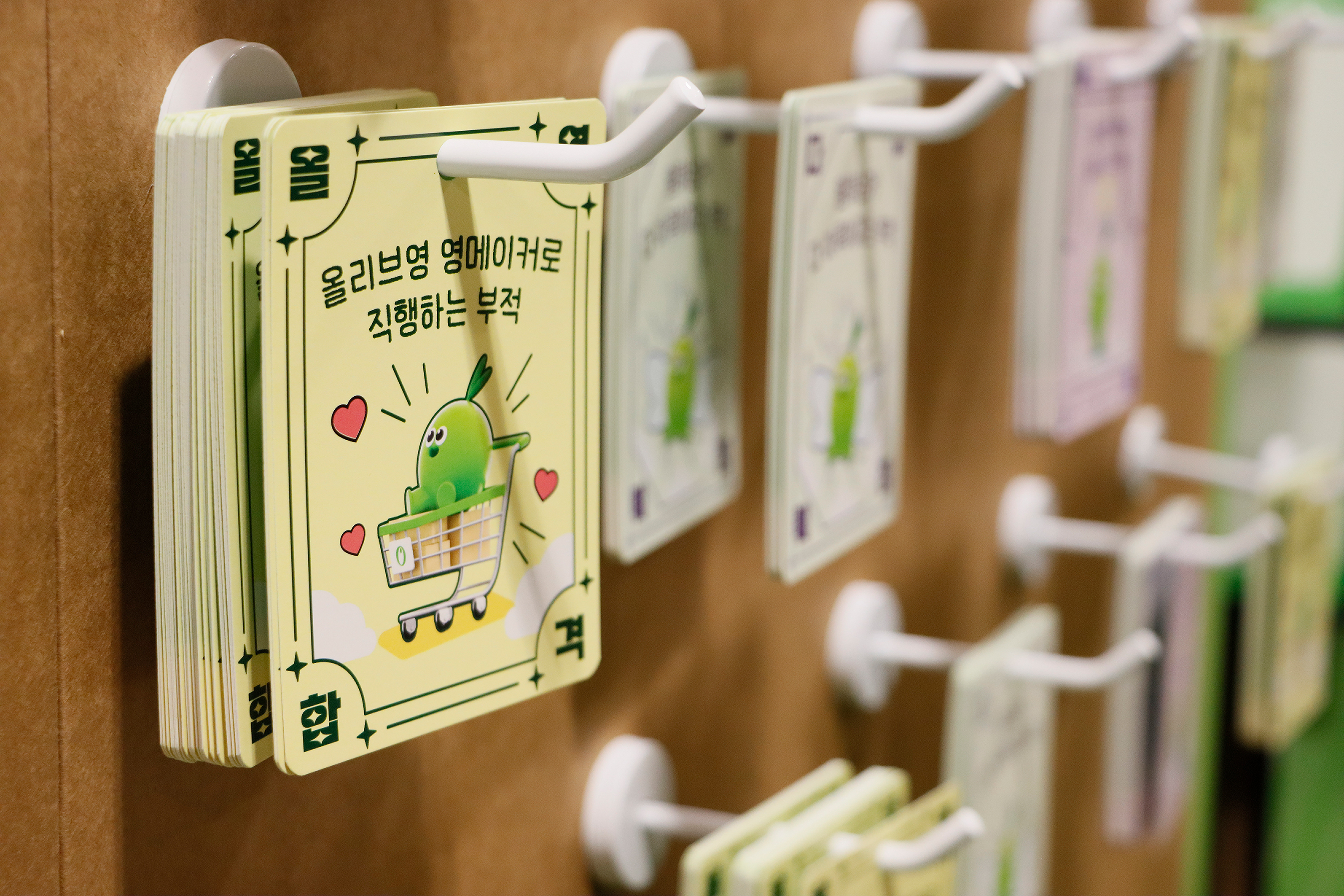 A yellow card with a green cartoon character in a shopping cart hangs on a wooden rack.