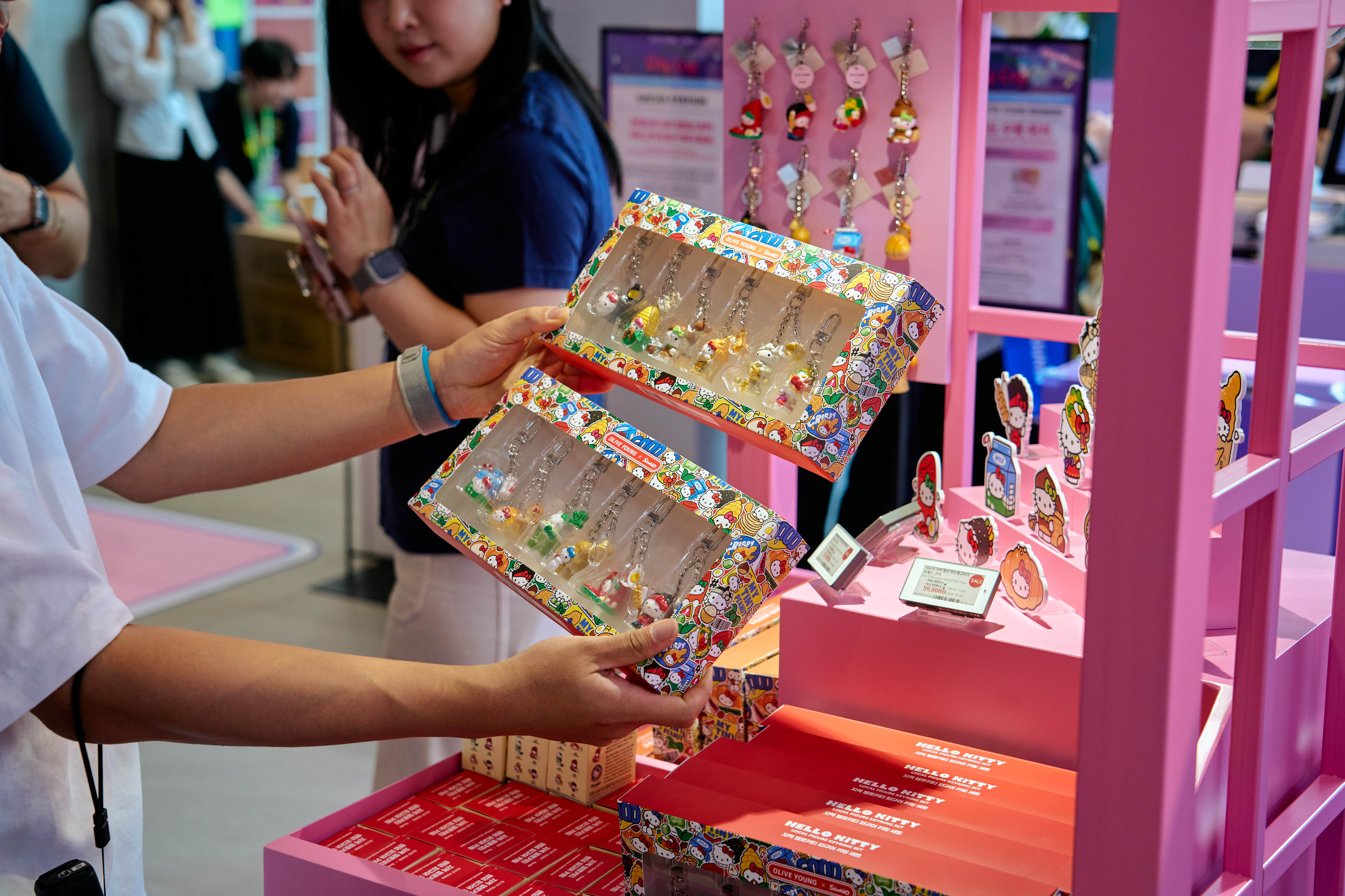 People examine Hello Kitty-themed jewelry at a pink retail display.