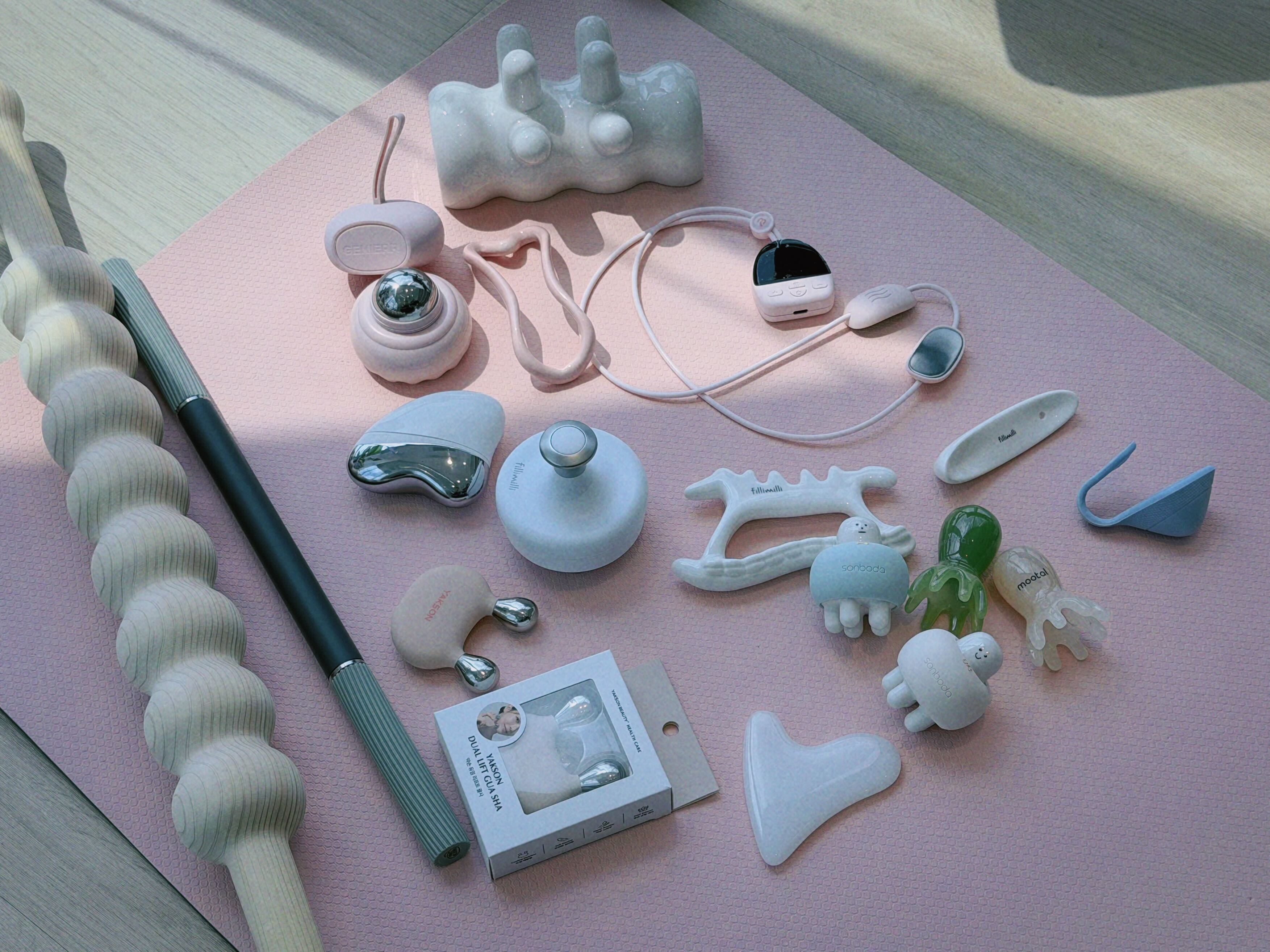 Various beauty and massage tools are arranged on a pink textured mat.