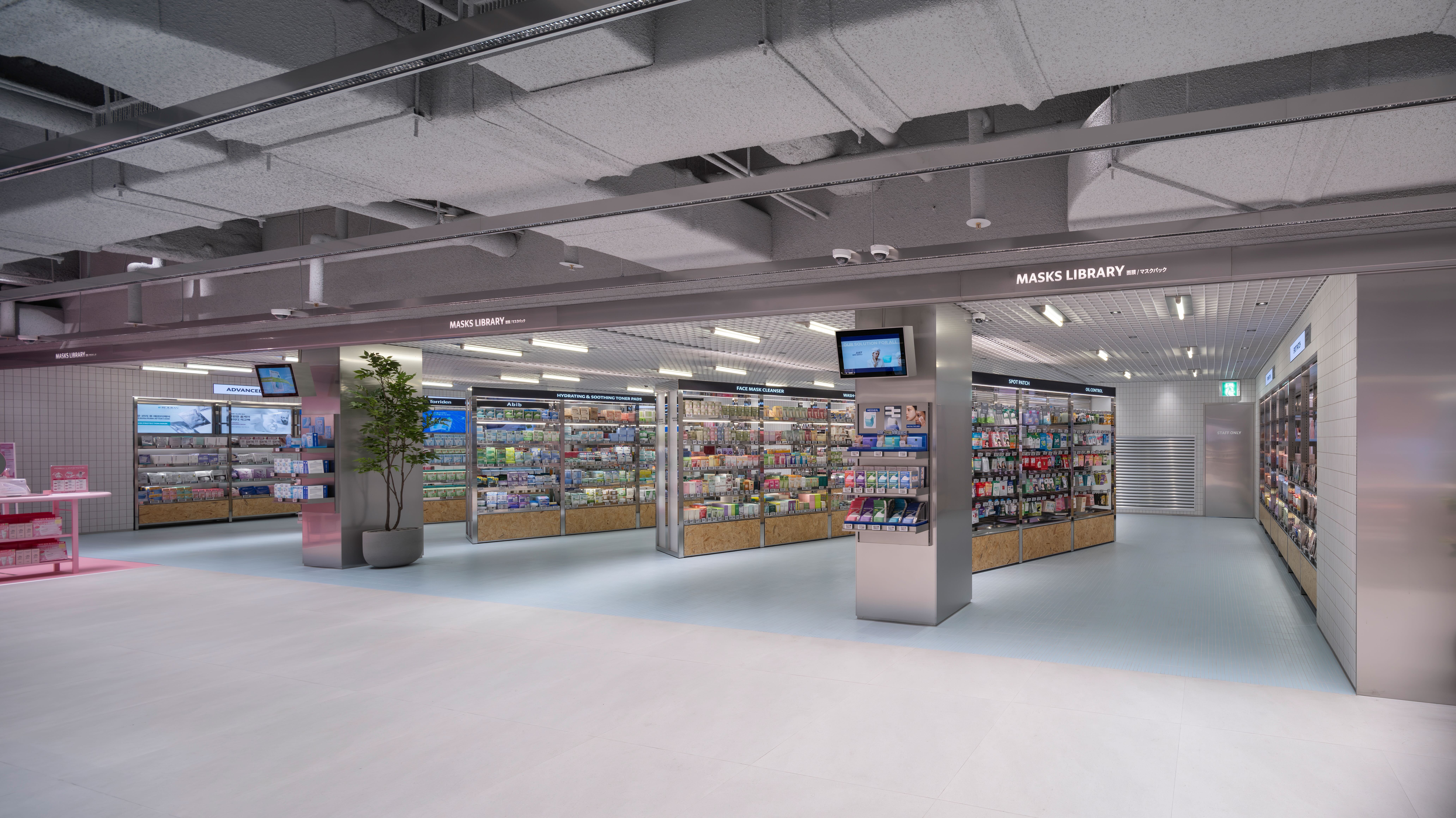 A brightly lit cosmetics store displays skincare products on shelves beneath a “MASKS LIBRARY” sign.