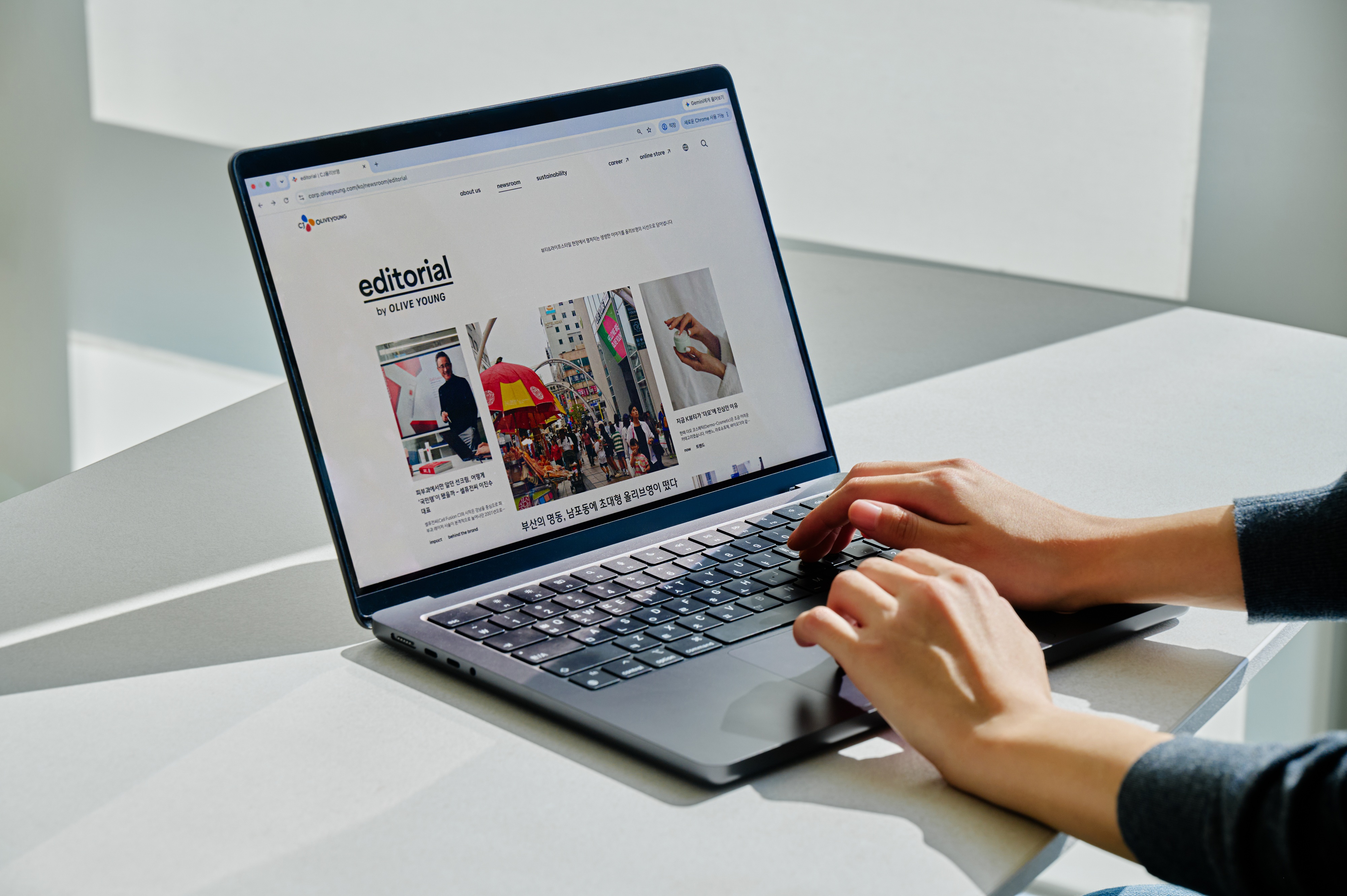 Hands type on a laptop displaying the Olive Young editorial webpage.