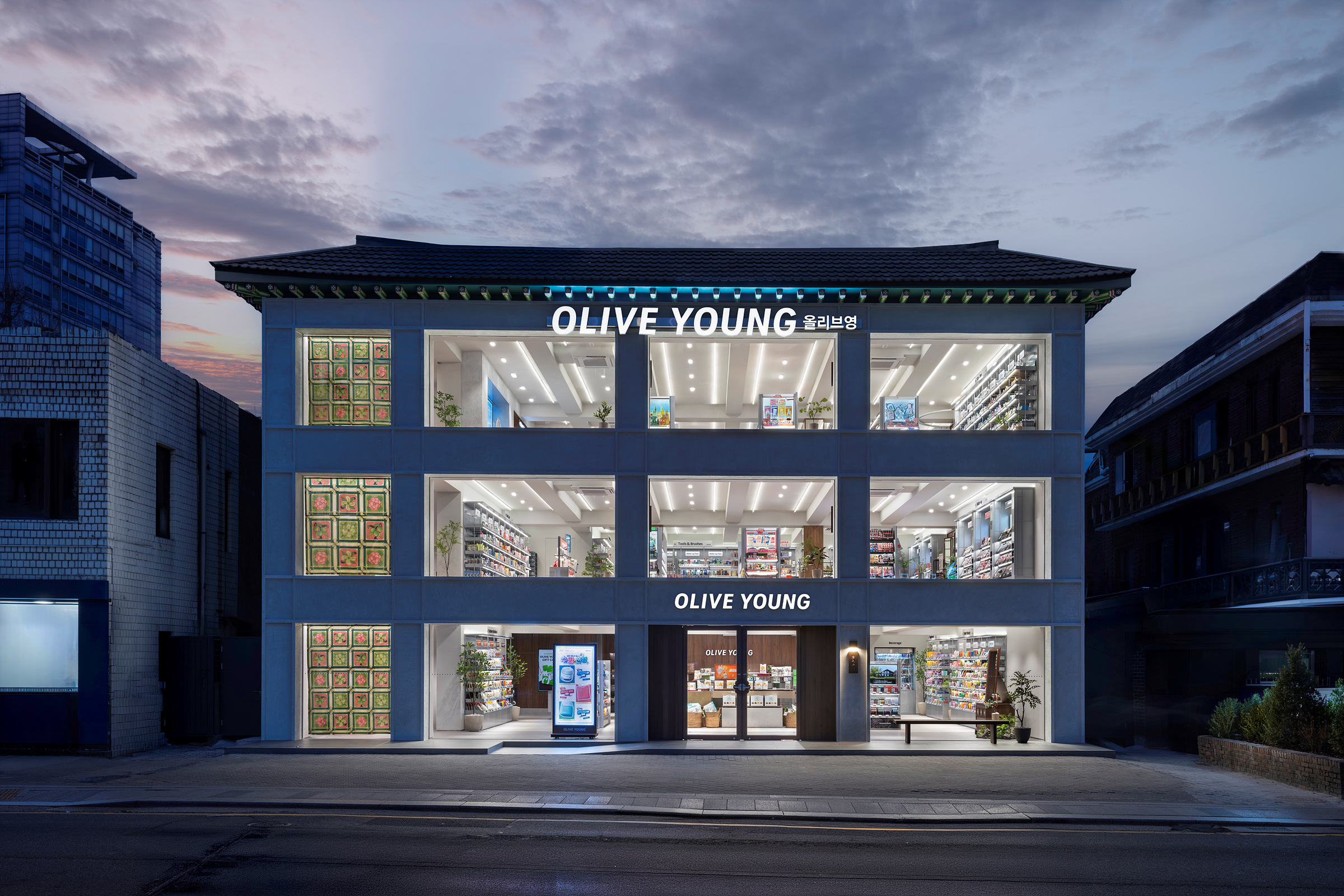 夕暮れの通りに建つ、伝統的な屋根を備えた3階建てのOLIVE YOUNG店舗。