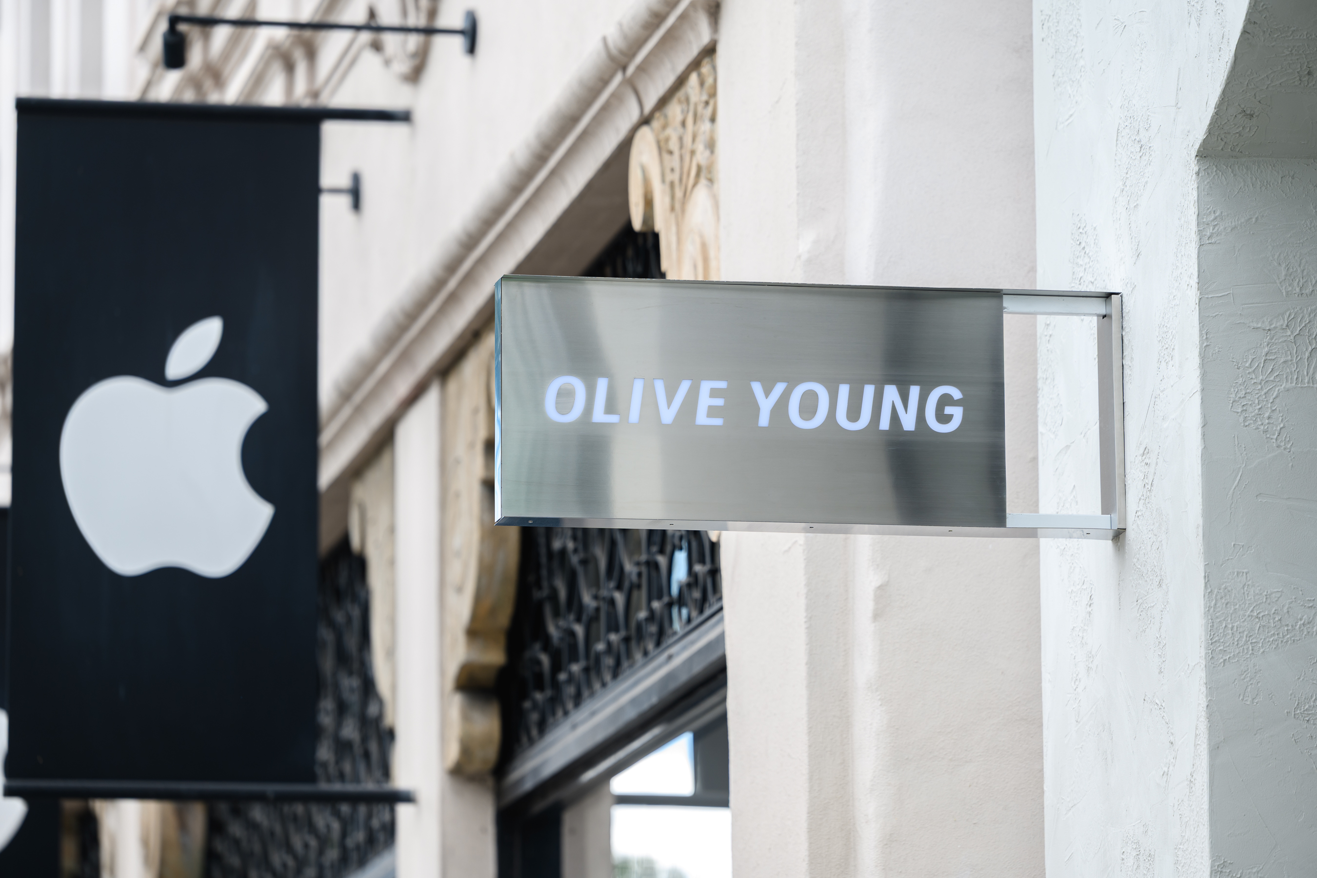 An illuminated OLIVE YOUNG storefront sign next to an Apple logo