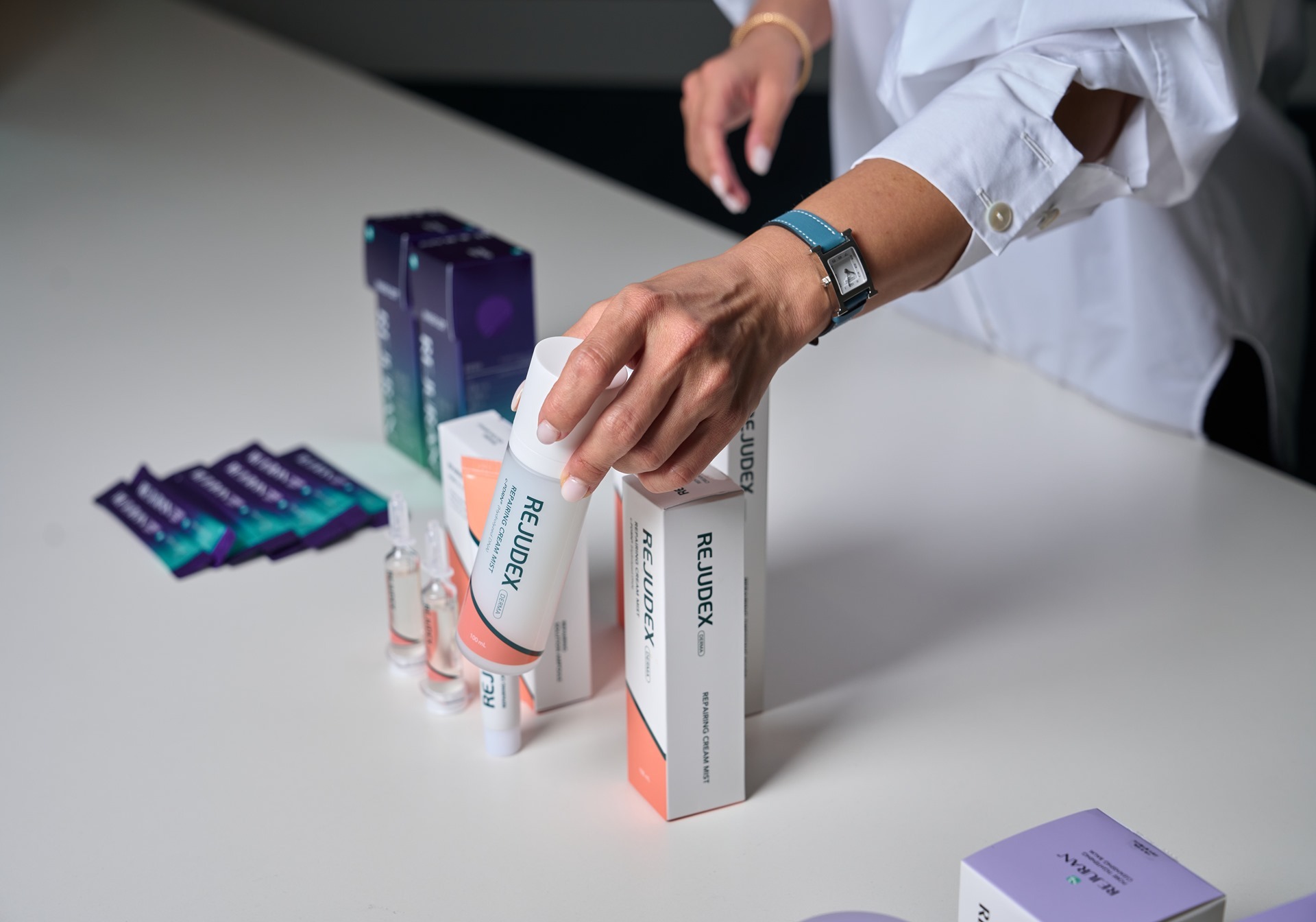 A person in a white shirt holds a Rejudex cream tube among boxes and ampoules on a table.