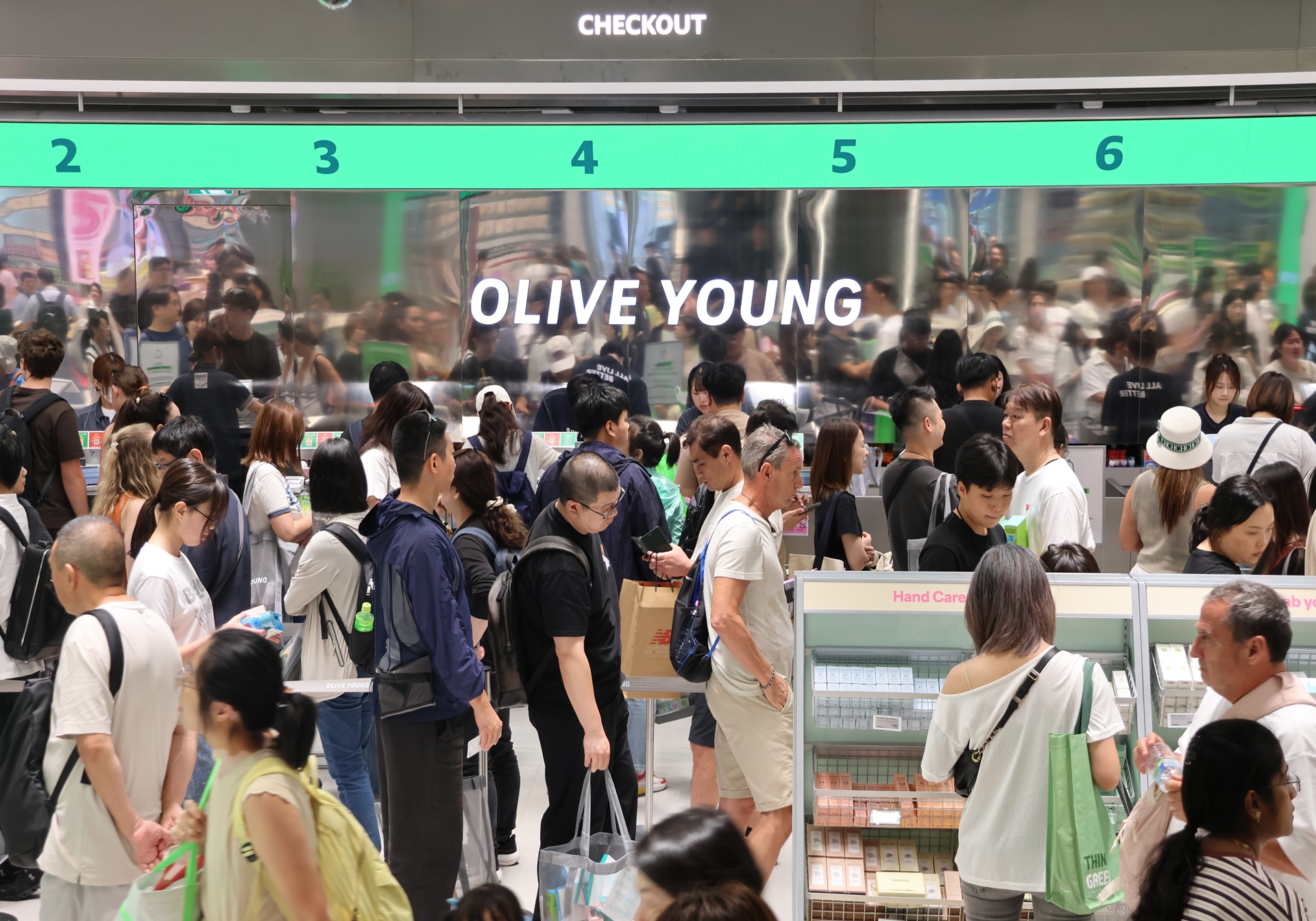 올리브영 매장 계산대 앞에 많은 사람들이 줄을 서 있으며 ‘CHECKOUT’과 번호가 보인다.