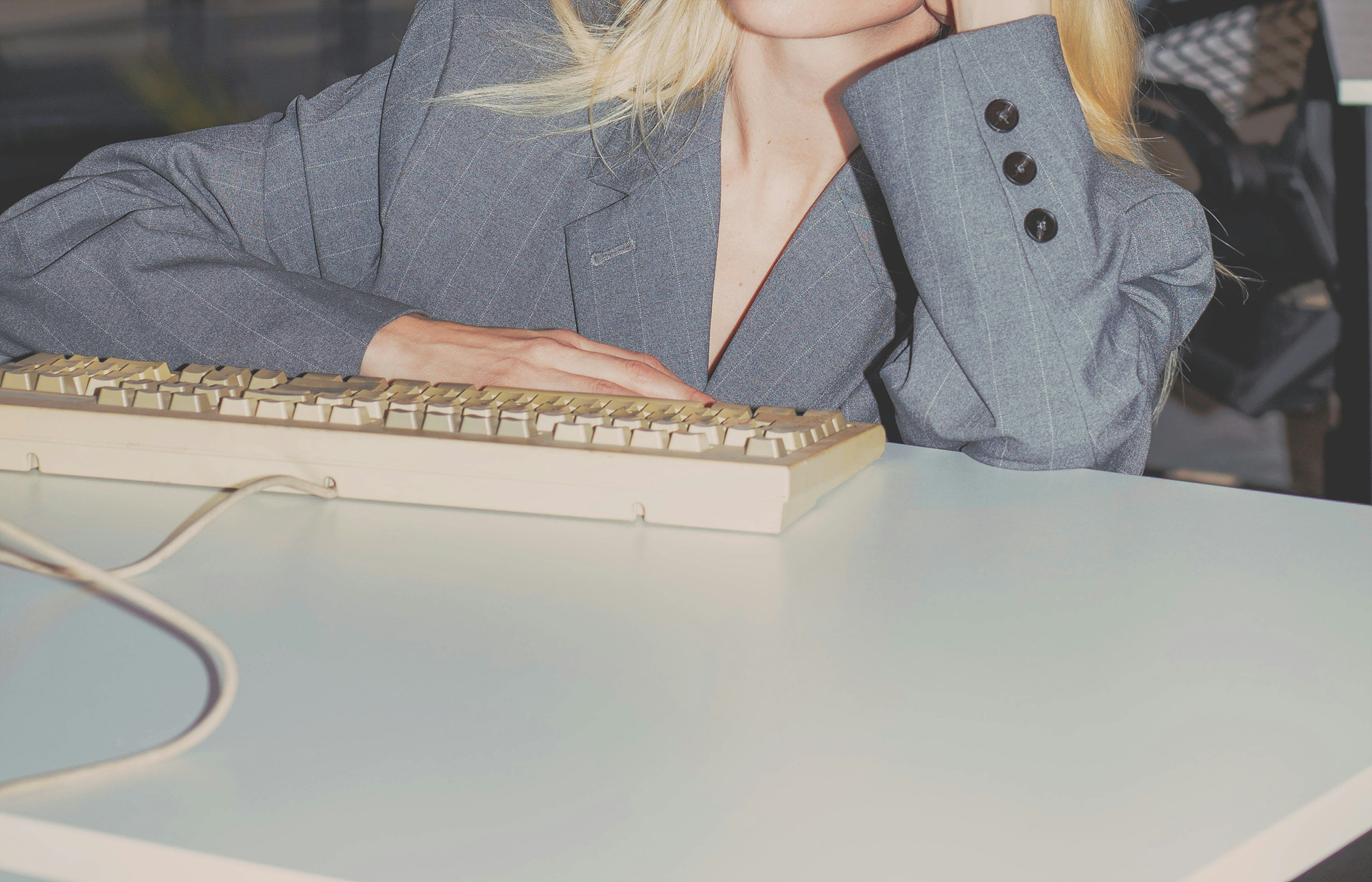 A person in a gray blazer rests one hand on a vintage computer keyboard.