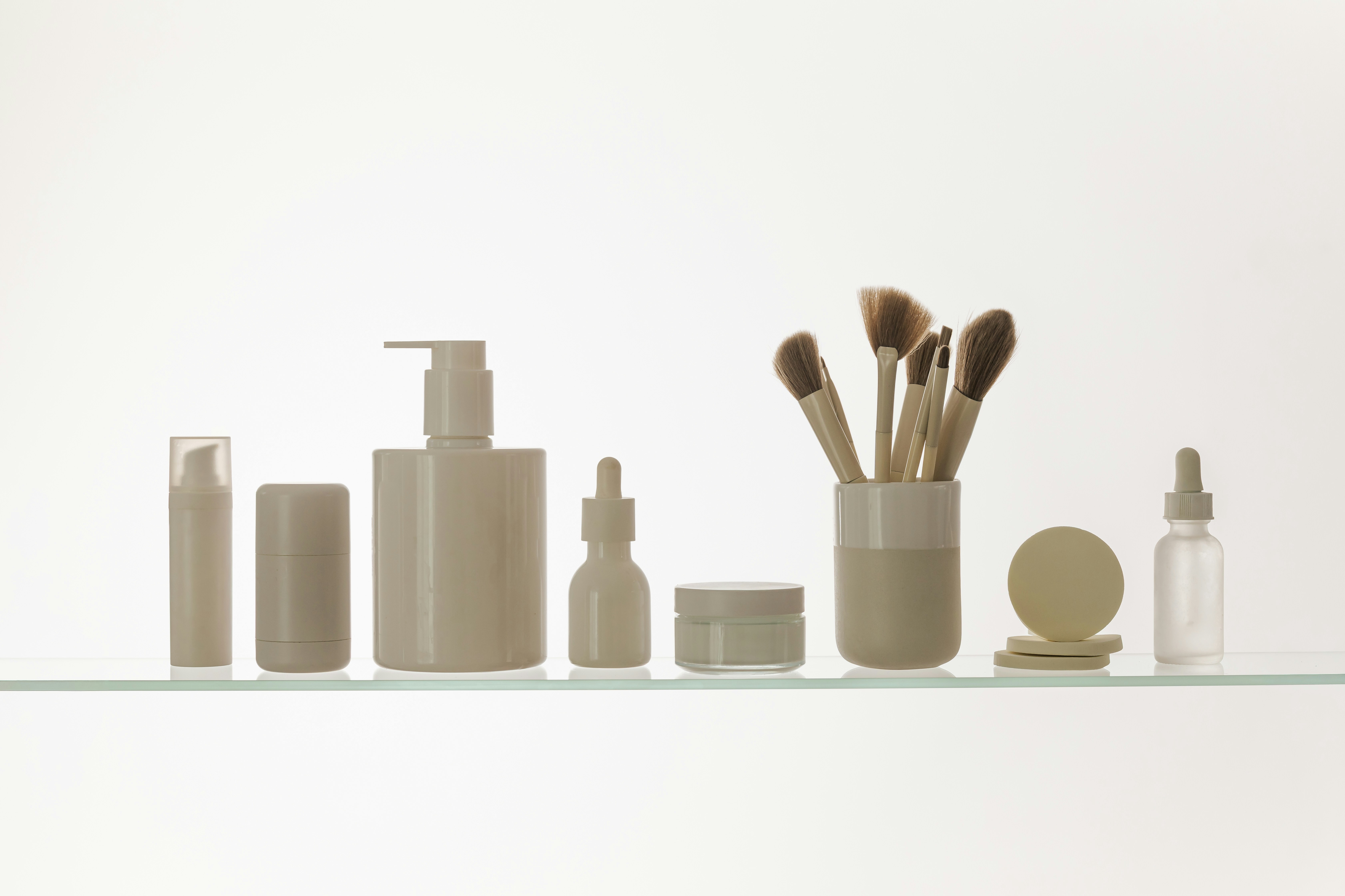 Skincare bottles and makeup brushes arranged on a white shelf.