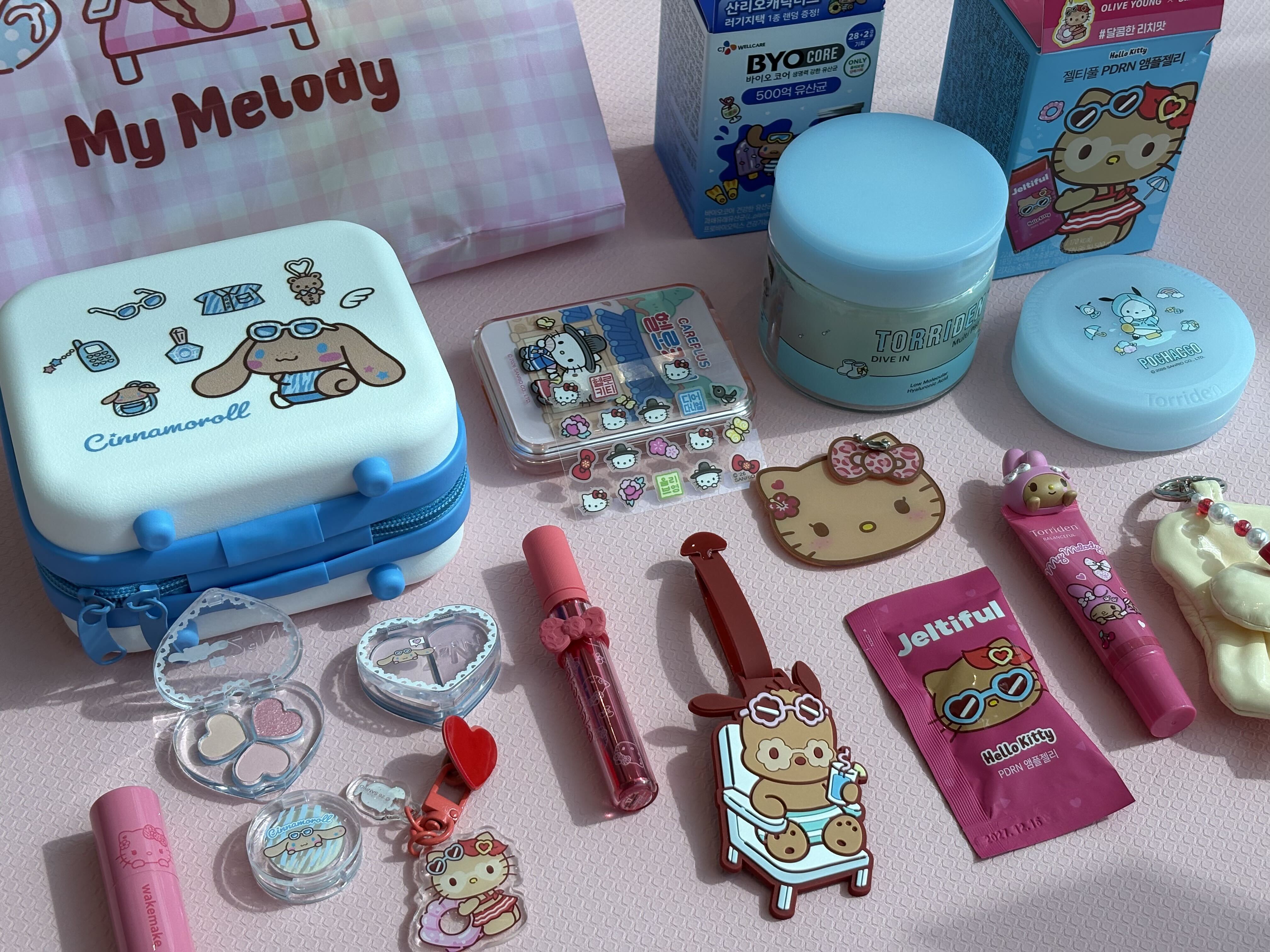 Sanrio character merchandise, cosmetics, cases, and accessories arranged on a pink tabletop.